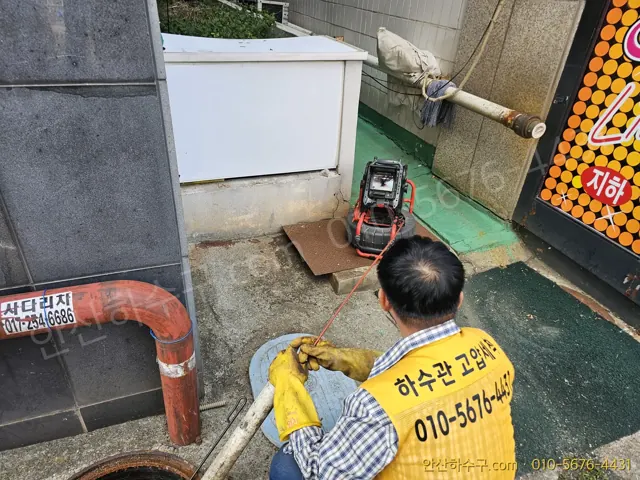 안산하수구 노란 조끼 작업자가 맨홀 앞에서 배관 내시경 모니터로 하수관 내부를 확인하는 모습