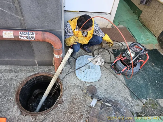 노란 조끼 작업자가 열린 맨홀에 배관 내시경 카메라 케이블을 넣는 현장